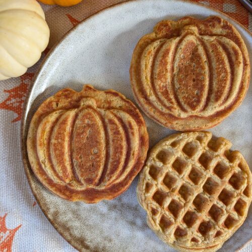 A plate with mini pumpkin yeast waffles, two sides showing a pumpkin inprint and one side showing a regular waffle pattern.