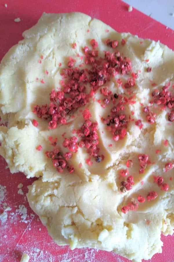 Pink peppercorns in cookie dough on a red plastic cutting board