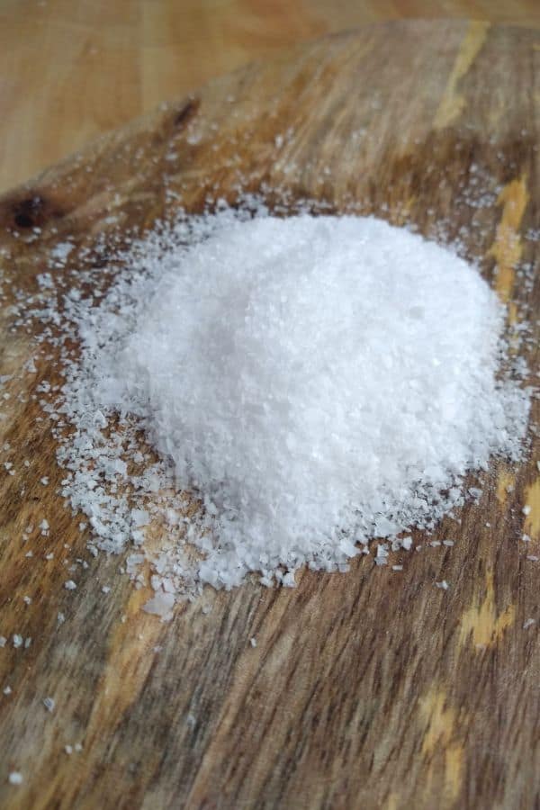 Kosher salt sitting on a wood board.