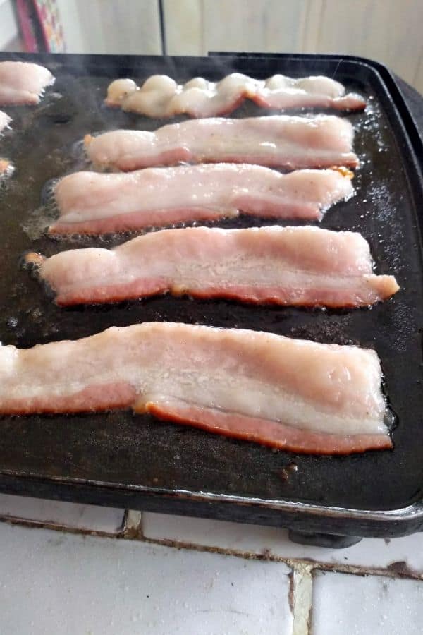 Raw Bacon cut in half on an electric griddle