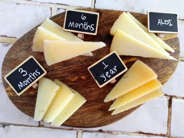 A Manchego cheese board with 3 month, 6 month, 1 year, and ALDI cheeses all cut into triangles on top of a wood cutting board.