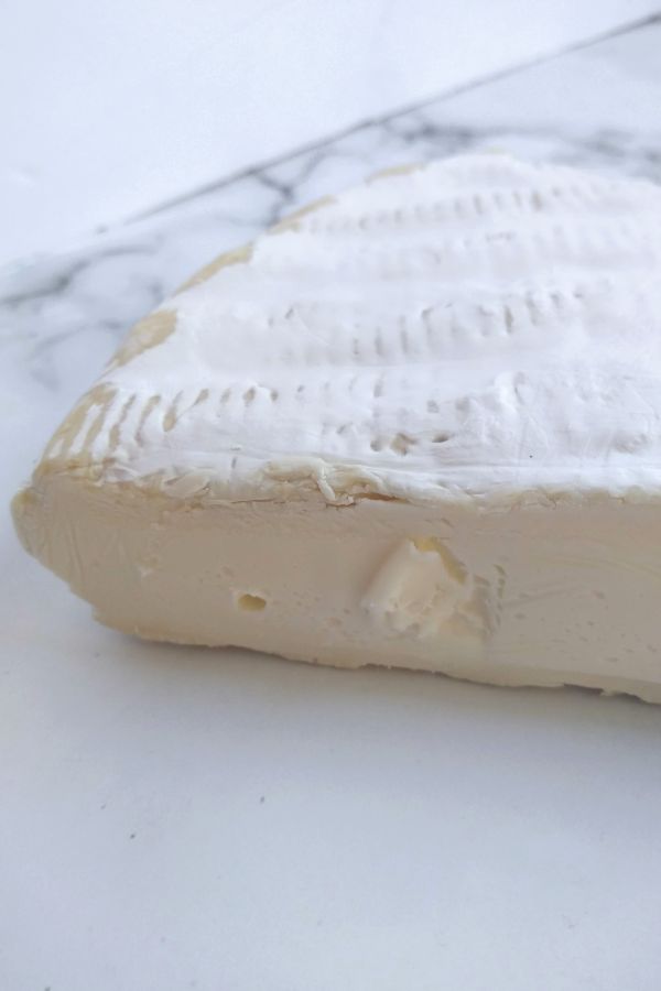 A side shot of Brie cheese sitting on a counter