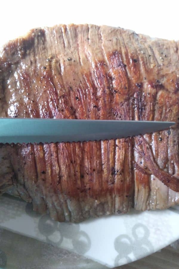 A close up of a flank steak that shows the grain with a knife next to it, demonstrating how to slice against the grain.