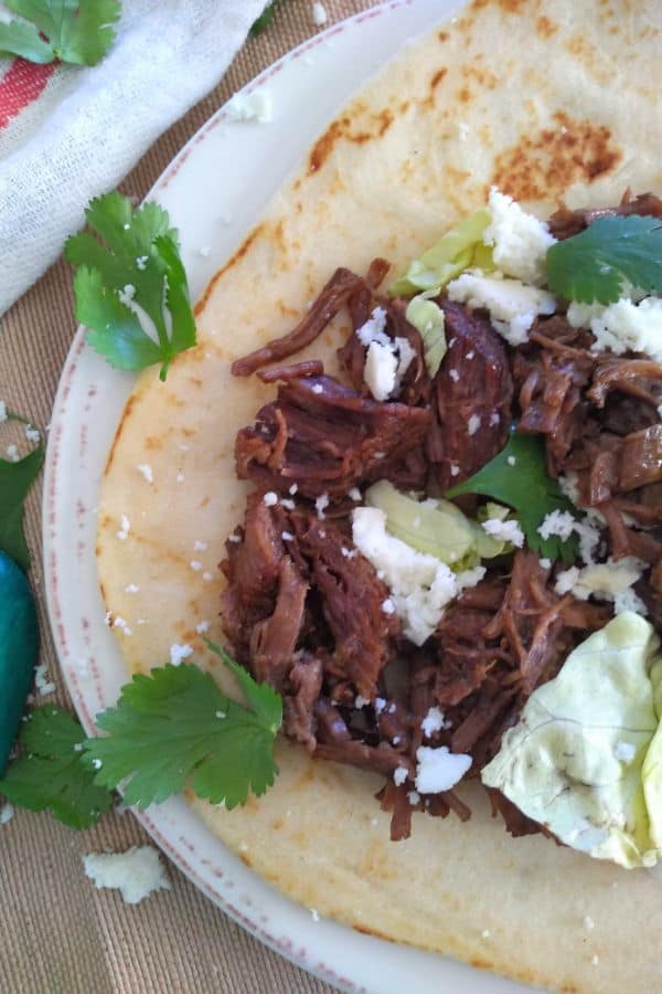 Chuck blade steak cooked for shredded beef and served on a flour tortillas as a taco with cheese, cilantro, lettuce