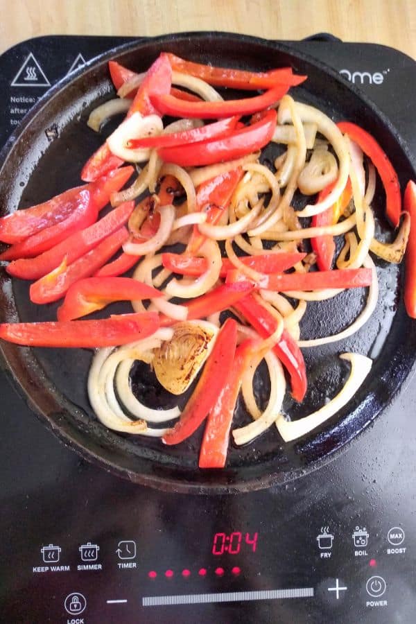 Onions and peppers on a cast iron skillet cooked on an induction cooktop