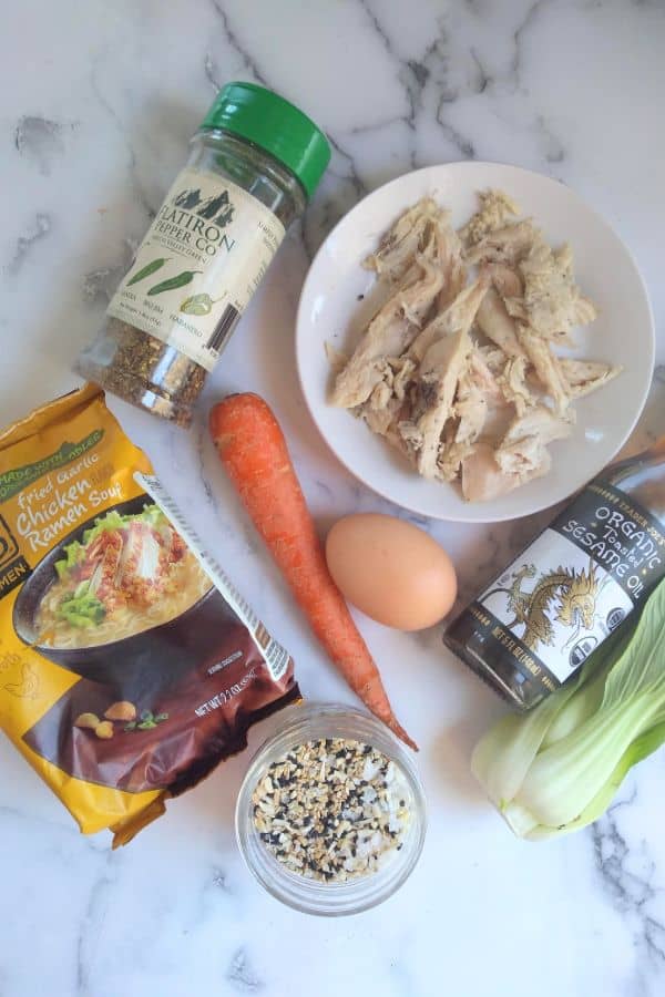 The ingredients for the soup on a counter top. They include leftover turkey, fried garlic chicken ramen soup, 1 small carrot, 1 large egg, toasted sesame oil, baby bok choy, and green pepper flakes.