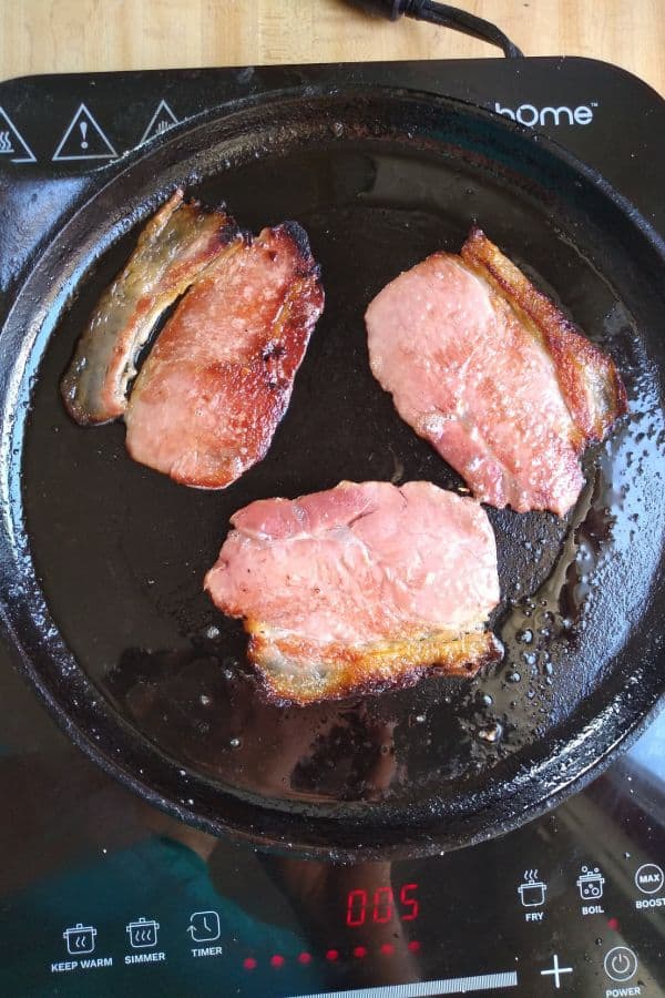 Back bacon being cooked on a cast iron griddle on a black induction burner.