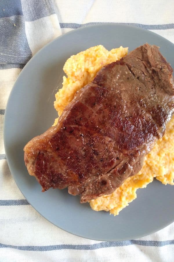 A sous vide and seared chuck blade steak served on top of grits on a bluish gray plate.