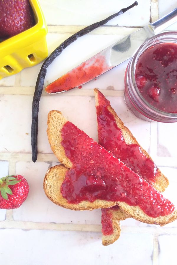 Strawberry Vanilla jam on two pieces of sliced toast with strawberries and a vanilla bean in the background