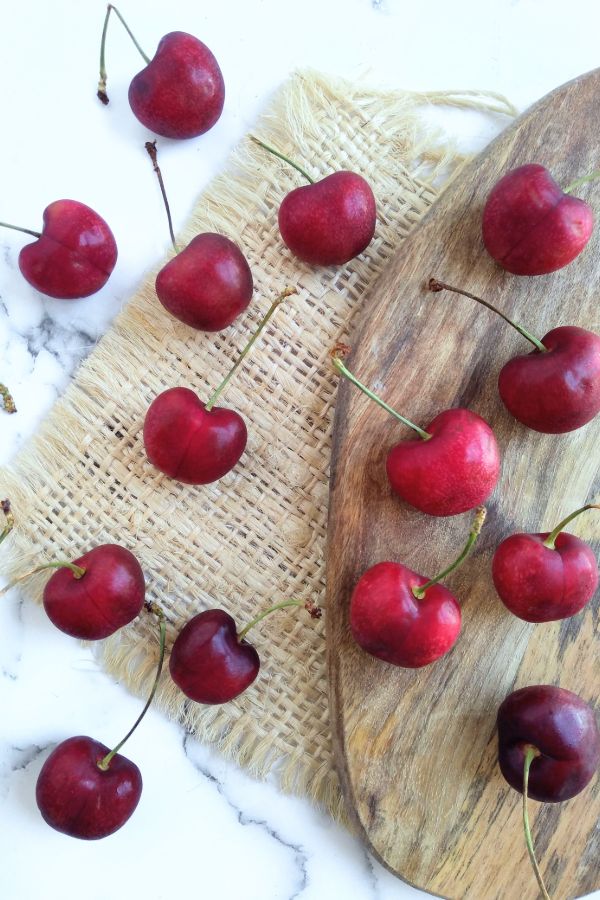 Audra Rose cherries sitting on a cutting board with a burlap cutout and a white title underneath