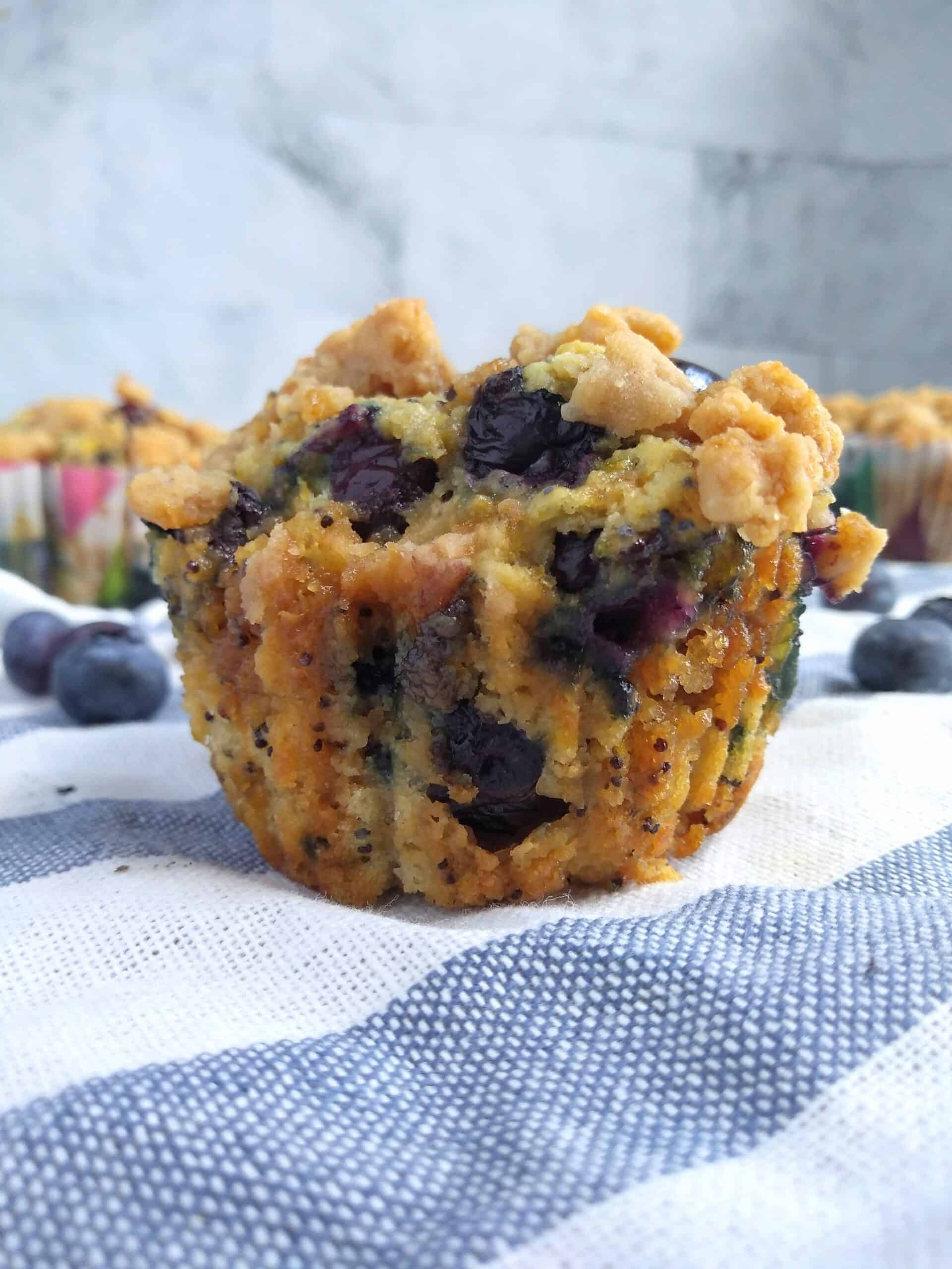 A single lemon poppyseed muffin with blueberries inside on top of a white towel with blue stripes. 