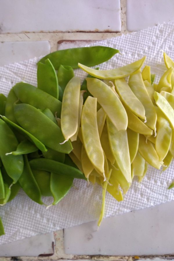 Green and yellow snow peas on a towel on a table.