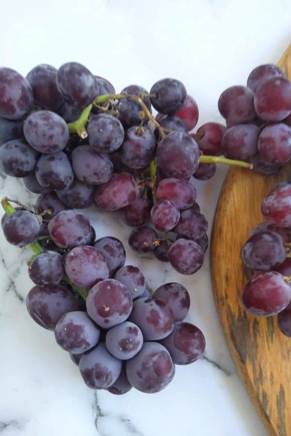 Candy snaps grapes sitting mostly on a white surface but also on a wood cutting board