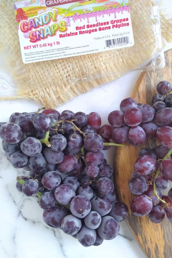 Candy Snaps grapes in bunches sitting on a white surface with a wood board next to it and the empty package as the top