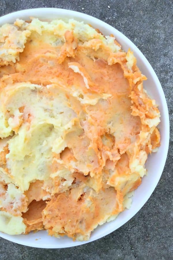 Marbled potatoes - a mix of white mashed potatoes and sweet potatoes in a white bowl on a stone surface.