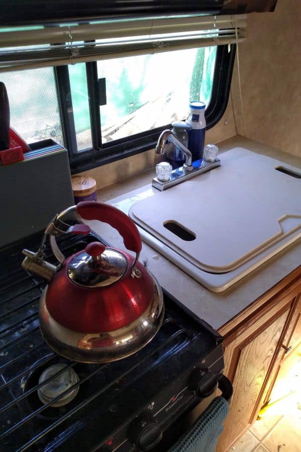 The kitchen inside a travel trailer with the sink covered with a cutting board.