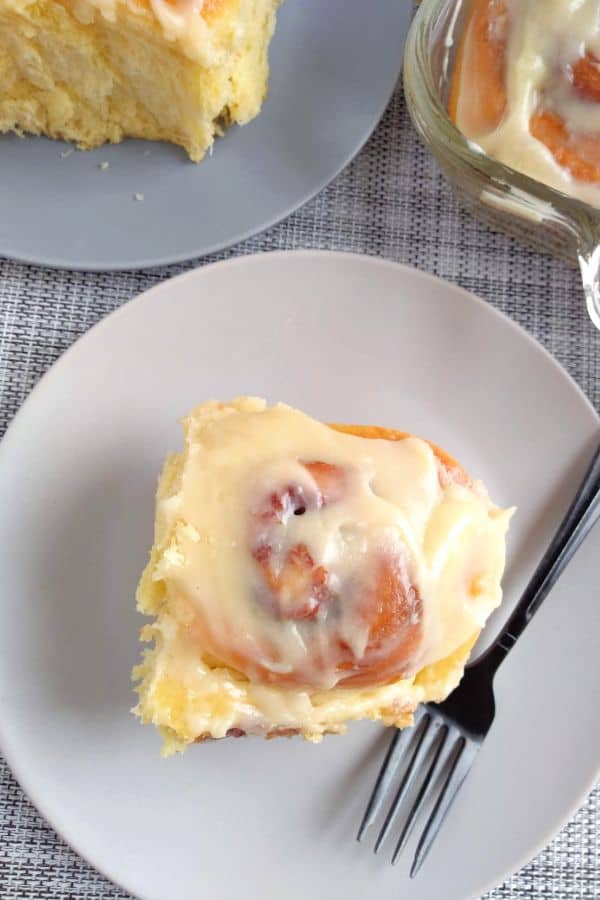 A cinnamon roll on top of a gray plate sitting on a gray textured place mat.