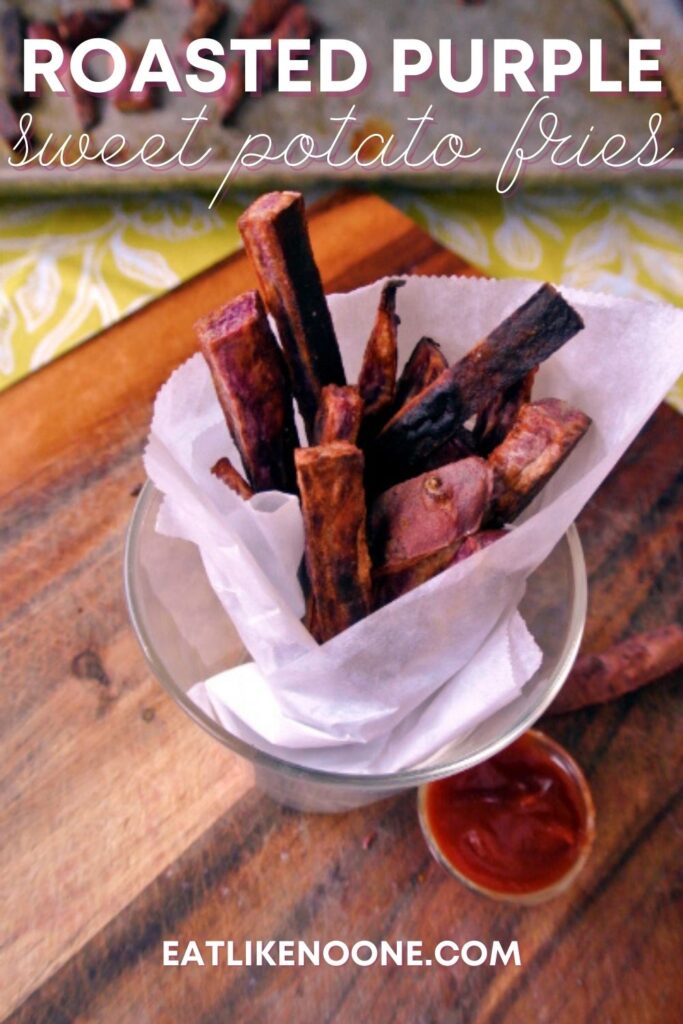 Purple sweet potato fries wrapped in parchment paper in a glass cup sitting on a wood cutitng board.