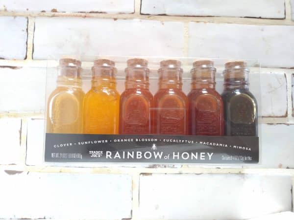 A Trader Joe's sampler set "Rainbow of Honey" with 6 different honeys arranged by color from light to dark sitting on a white tile counter.