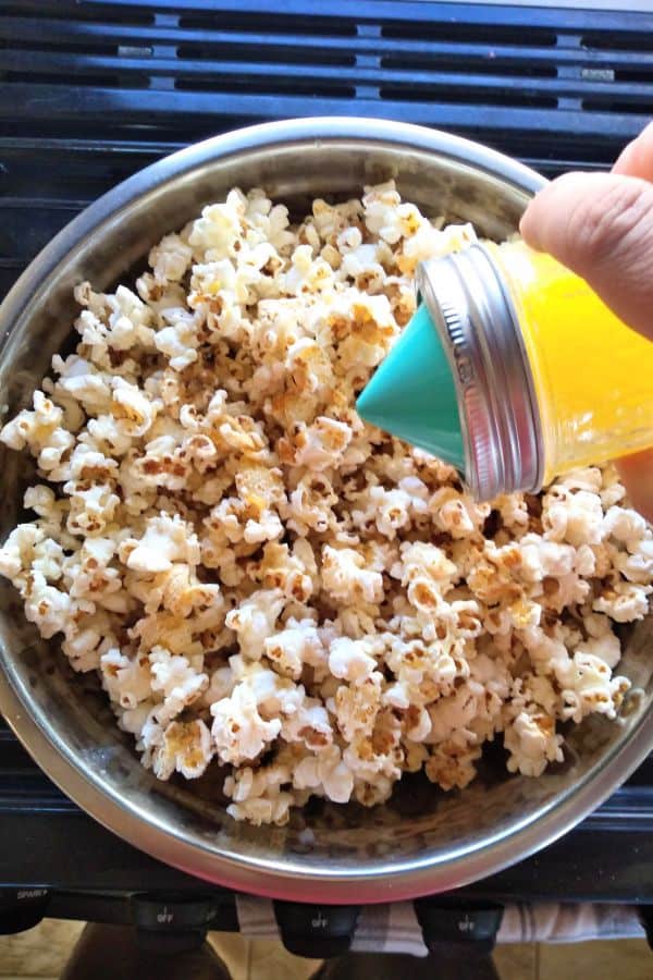 The Ergo Spout mini is attached to a mason jar full of butter and it's been poured onto a metal bowl full of popcorn.