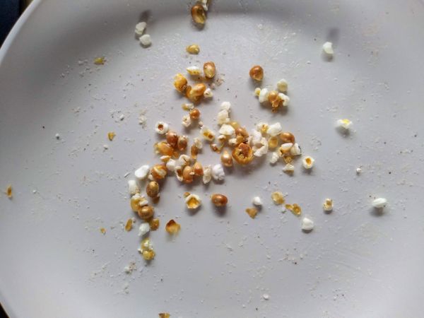 A bowl with a few unpopped popcorn kernels and some small piece of popped popcorn.