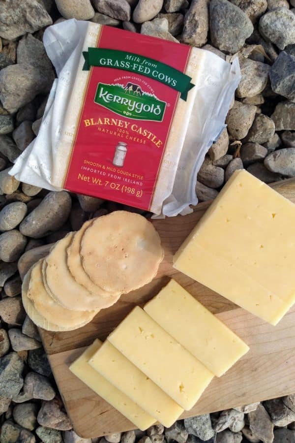 Slices of Blarney Castle cheese on a wood cutting board with some crackers and a whole packaged block of cheese next to it.