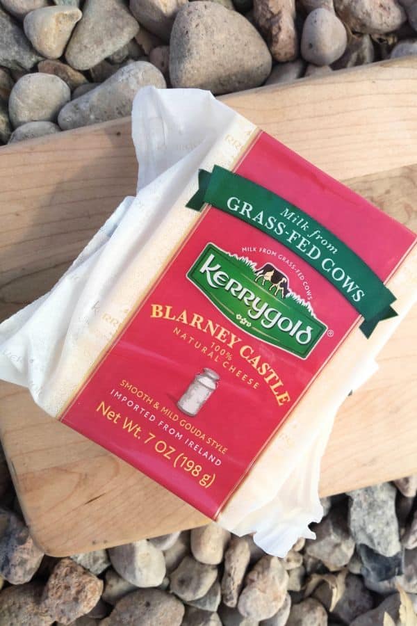 A block of Kerrygold Blarney Castle cheese in the package on a wood cutting board on top of some rocks.