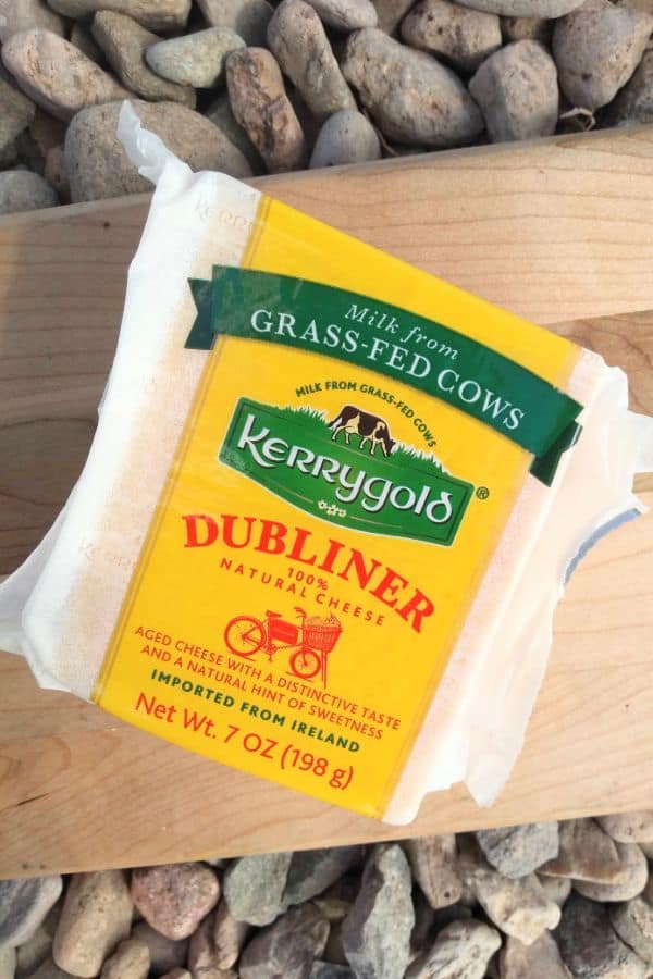 Kerrygold Dubliner cheese in it's package on top of a wood cutting board on top of some stones.