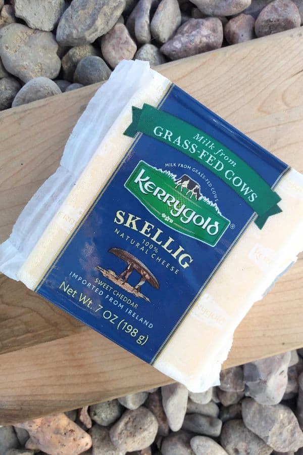 A picture of packaged Kerrygold Skellig sweet cheddar cheese on a wood cutting board on top of some rocks.