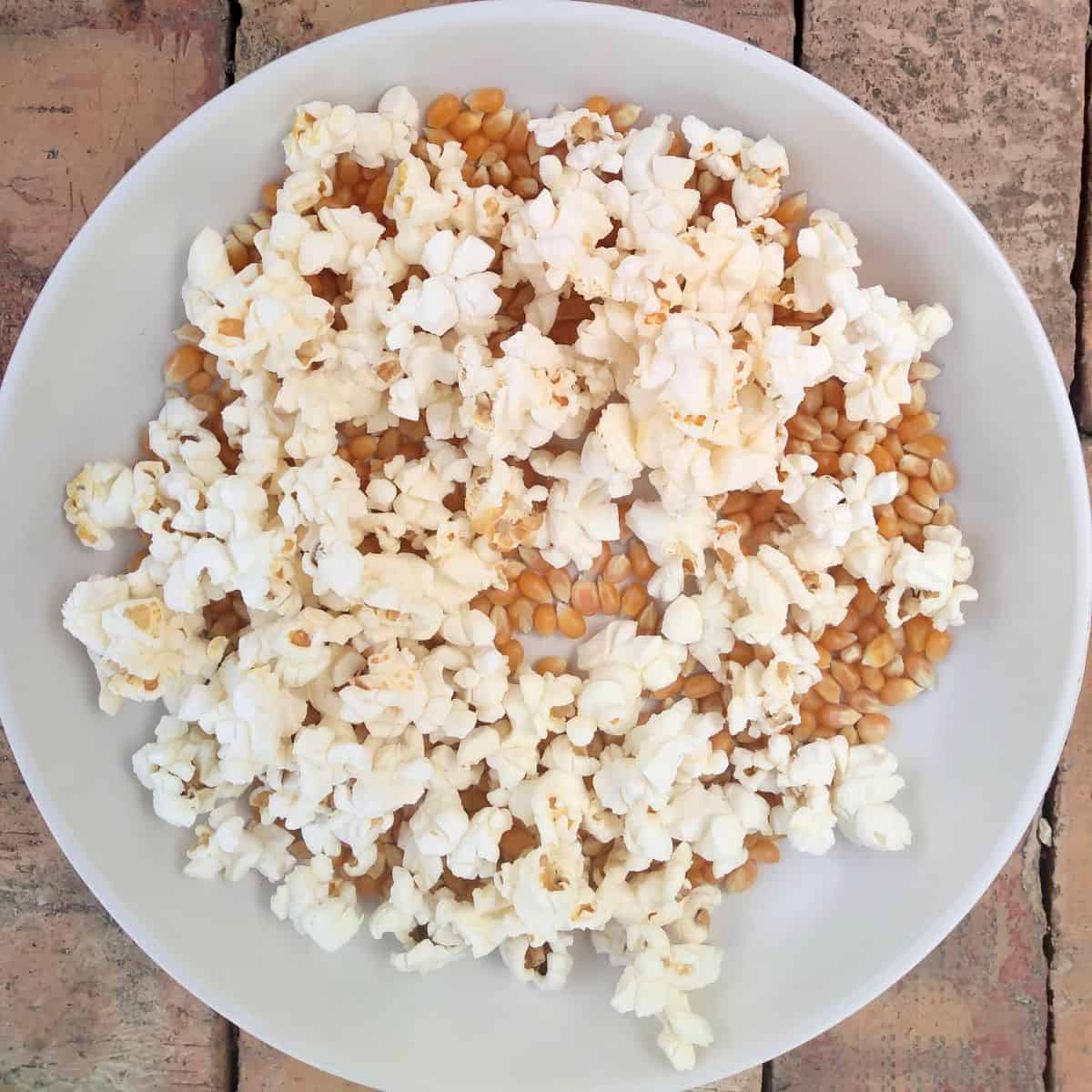 A bowl of popped popcorn and unpopped kernels sitting on a wood board.