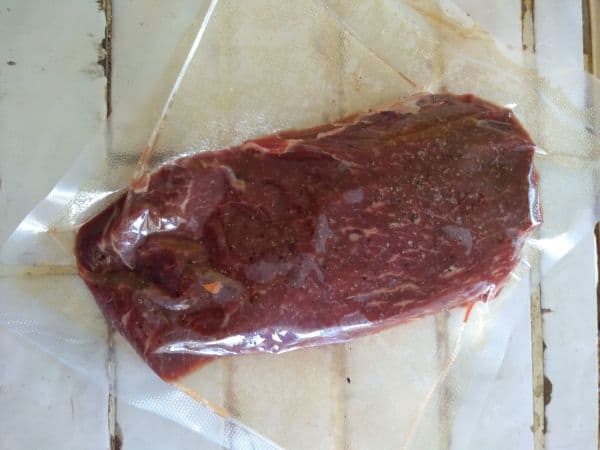 A vacuum sealed flat iron steak on top of a white tile countertop.