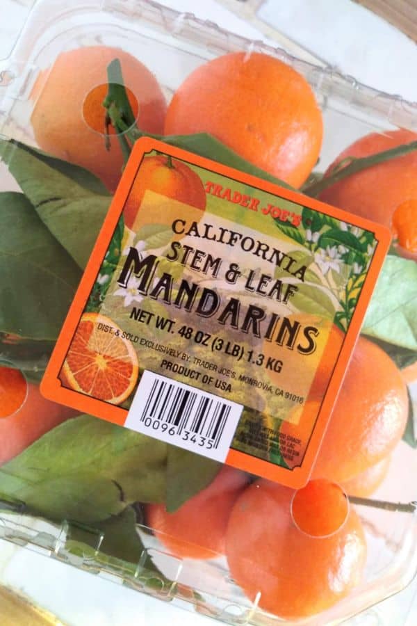 A plastic container of Trader Joe's California Stem and Leaf Mandarins sitting on a white counter.