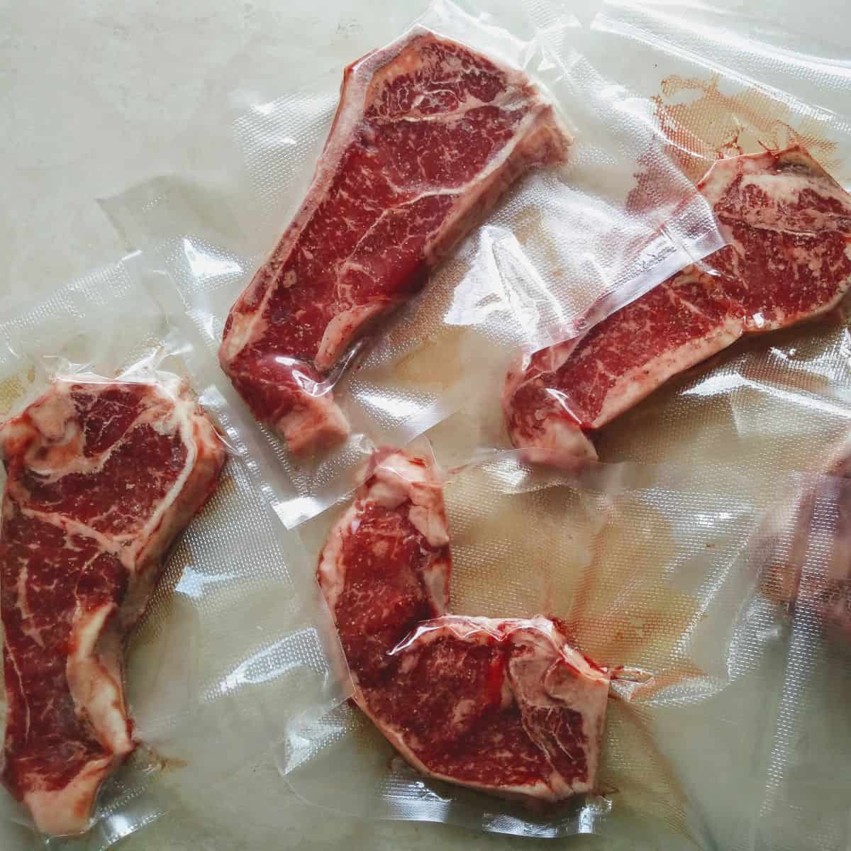 5 raw New York strips steaks that has been vacuum sealed in plastic, sitting on a camper table.