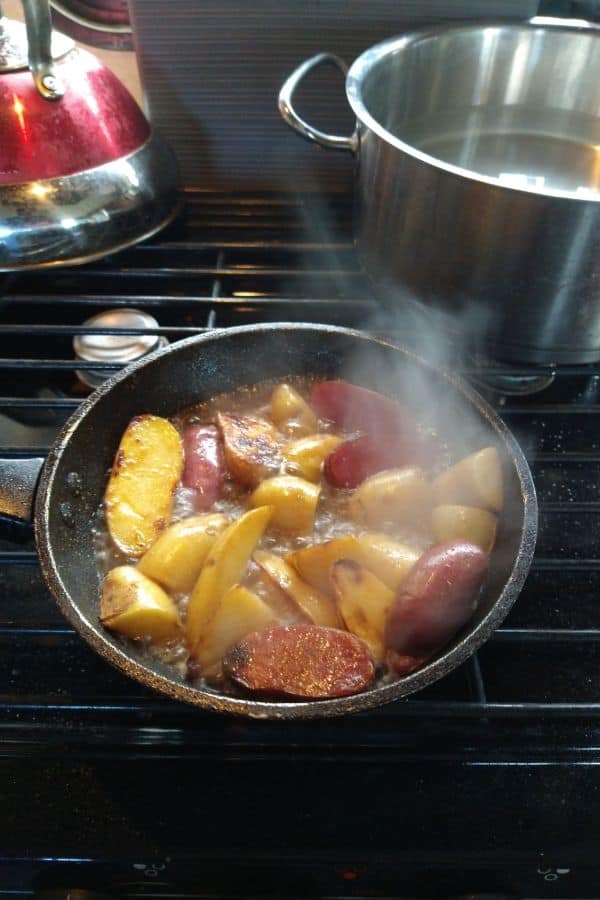 A camper stove top with a frying pan filling with fingerling potatoes and boiling water to help them get tender.