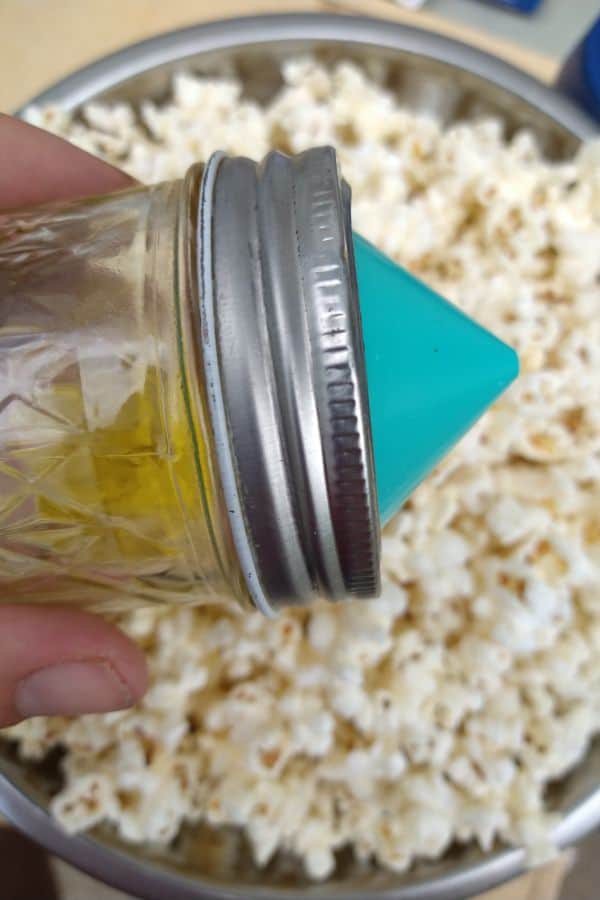 The Mini Ergo spout attached a small mason jar with olive oil in it, over top of a bowl of popcorn.