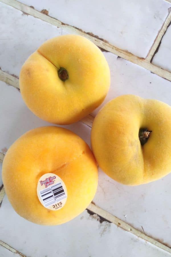 A set of three yellow Peach Pie donut peaches siting on a white tile counter.