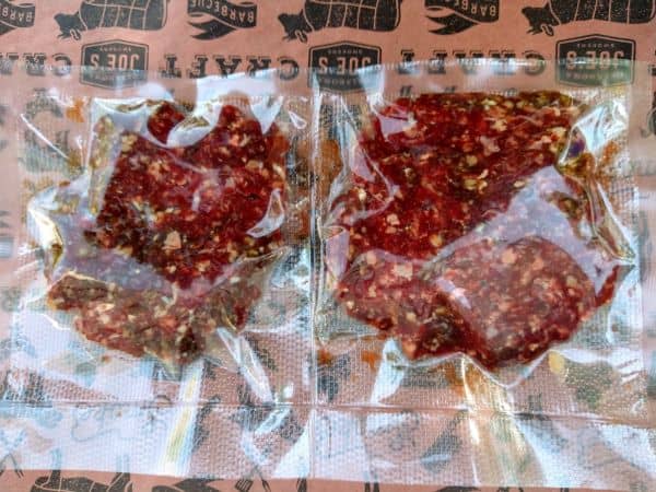 Two vacuum sealed burgers in a divided plastic pouch on top of a butcher paper 