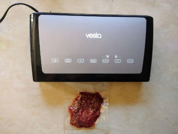 A Vesta vacuum sealer, sealing a single burger in a plastic bag. The sealer is sitting on a camper dinning table.