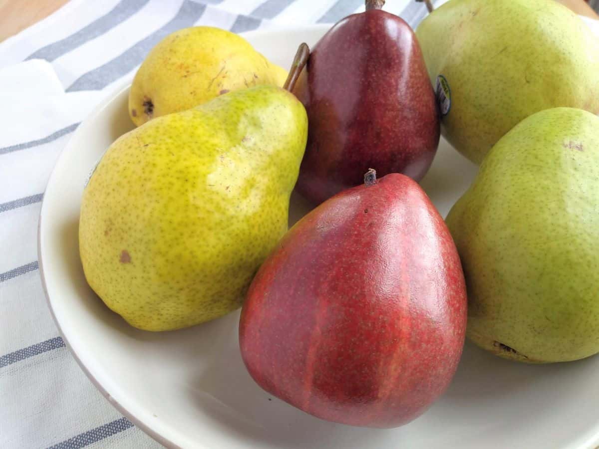 A bowl with two of each of these types of pears from left to right - Bartlett, Red D'Anjou, and D'Anjou. The bowl is on a blue striped towel.