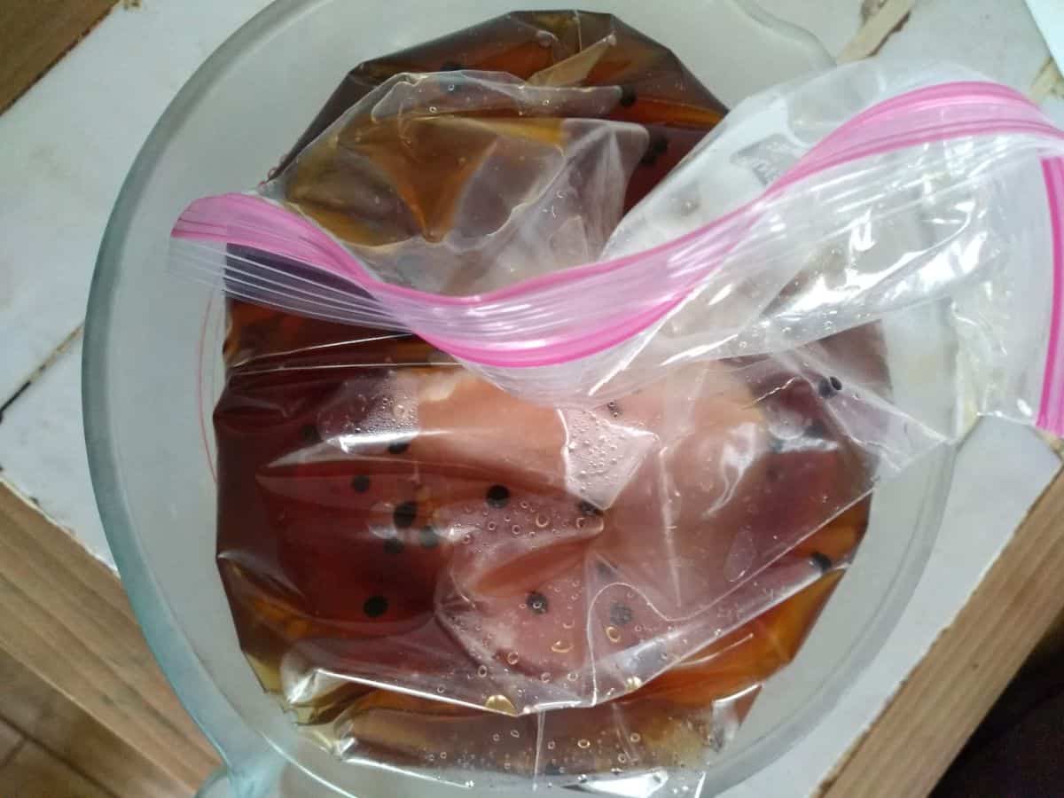 Pork chops in a plastic bag with a brine. The bag is inside a glass bowl on top of a white tile countertop.