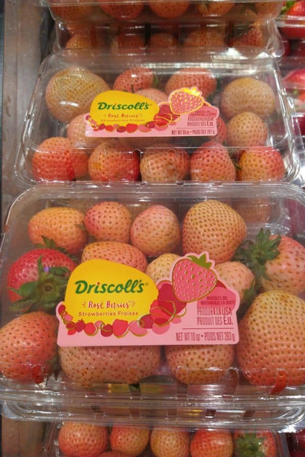 A display of Driscoll's Rosé strawberries at a grocery store. The berries are a link pink color and come in clear plastic 10 ounce package.