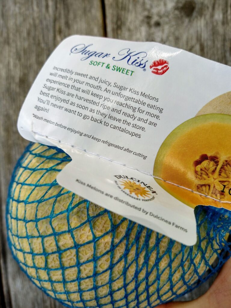 The Sugar Kiss melon comes wrapped in blue netting with a label that reads "Incredibly sweet and juicy, Sugar Kiss Melons will melt in your mouth. An unforgettable eating experience that will keep you reaching for more. Sugar Kiss are harvested ripe and ready and are best enjoyed as soon as they leave the store. You';; never want to go back to cantaloupes again!