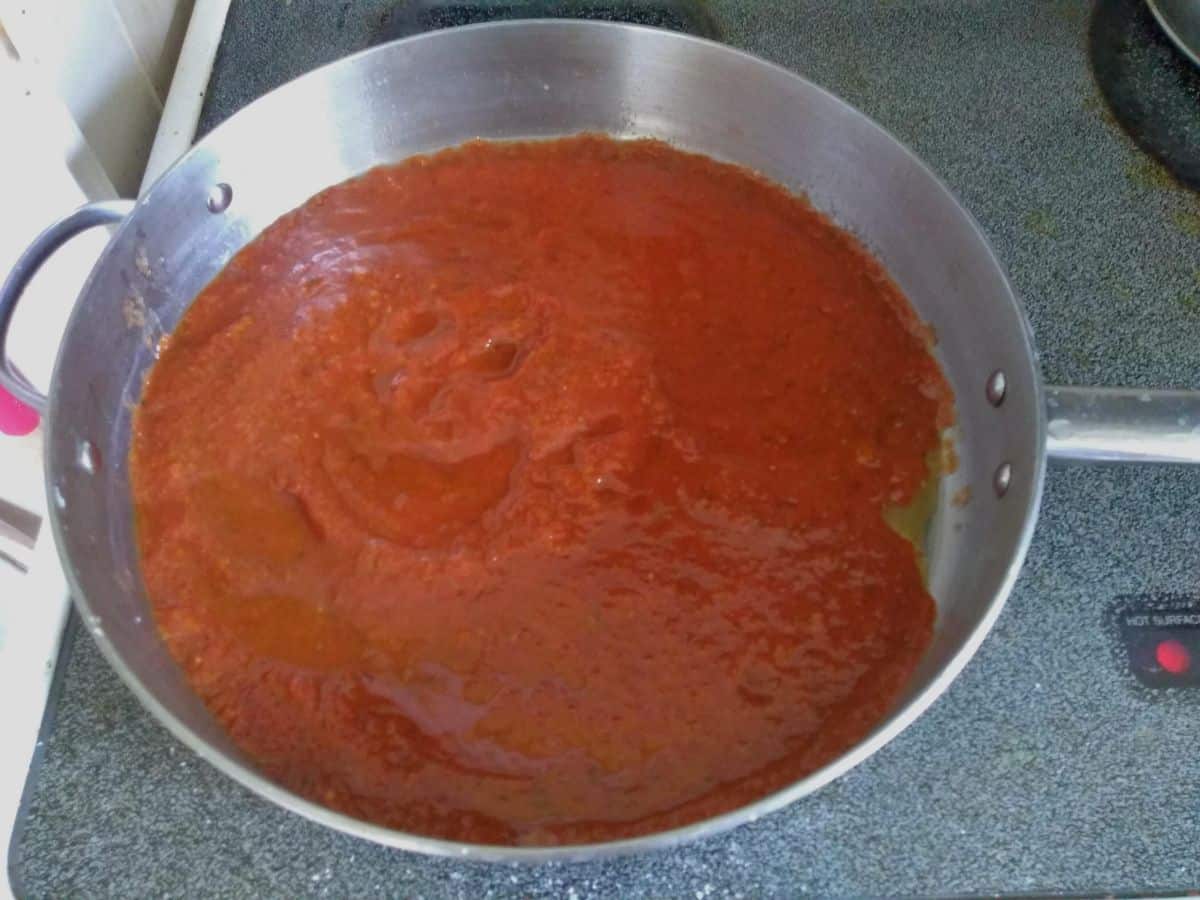A metal frying pan on the stove top with red tomato sauce that is done cooking inside.