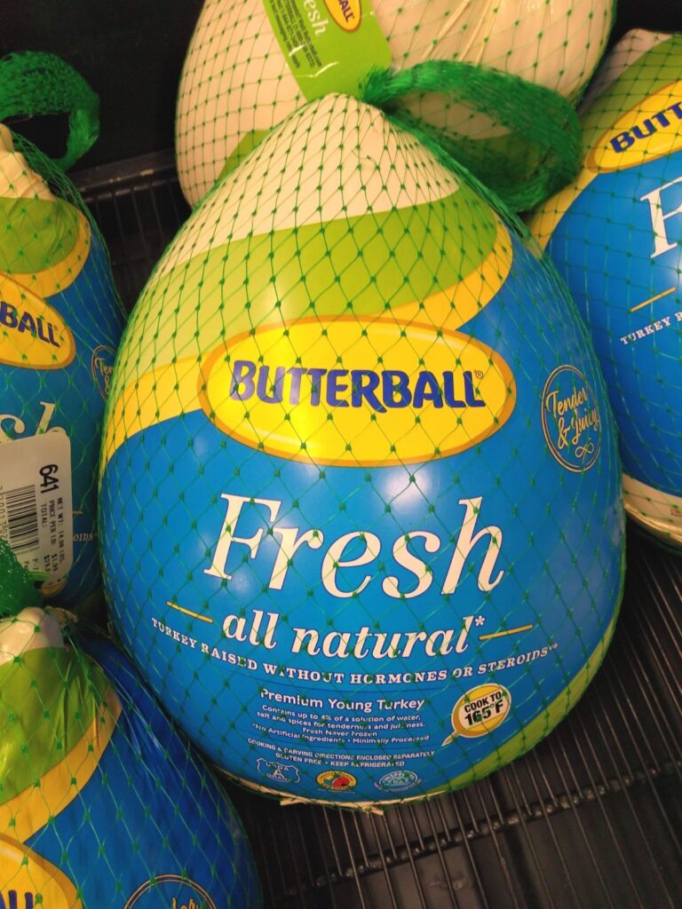 Packaged Butterball Fresh Turkeys with netting on them are sitting in a refrigerated case at the grocery store.