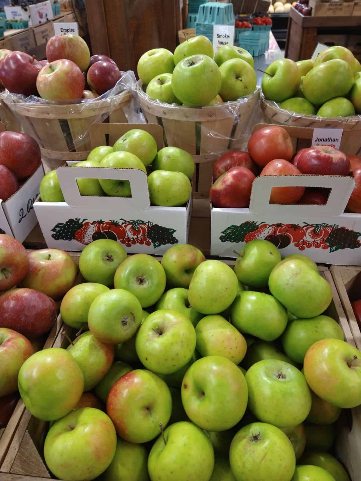 A display of both green and red colored apples. At the top the apples are in a bushel basket, in the middle are a smaller cardboard basket, and at the bottom the apples are loose.