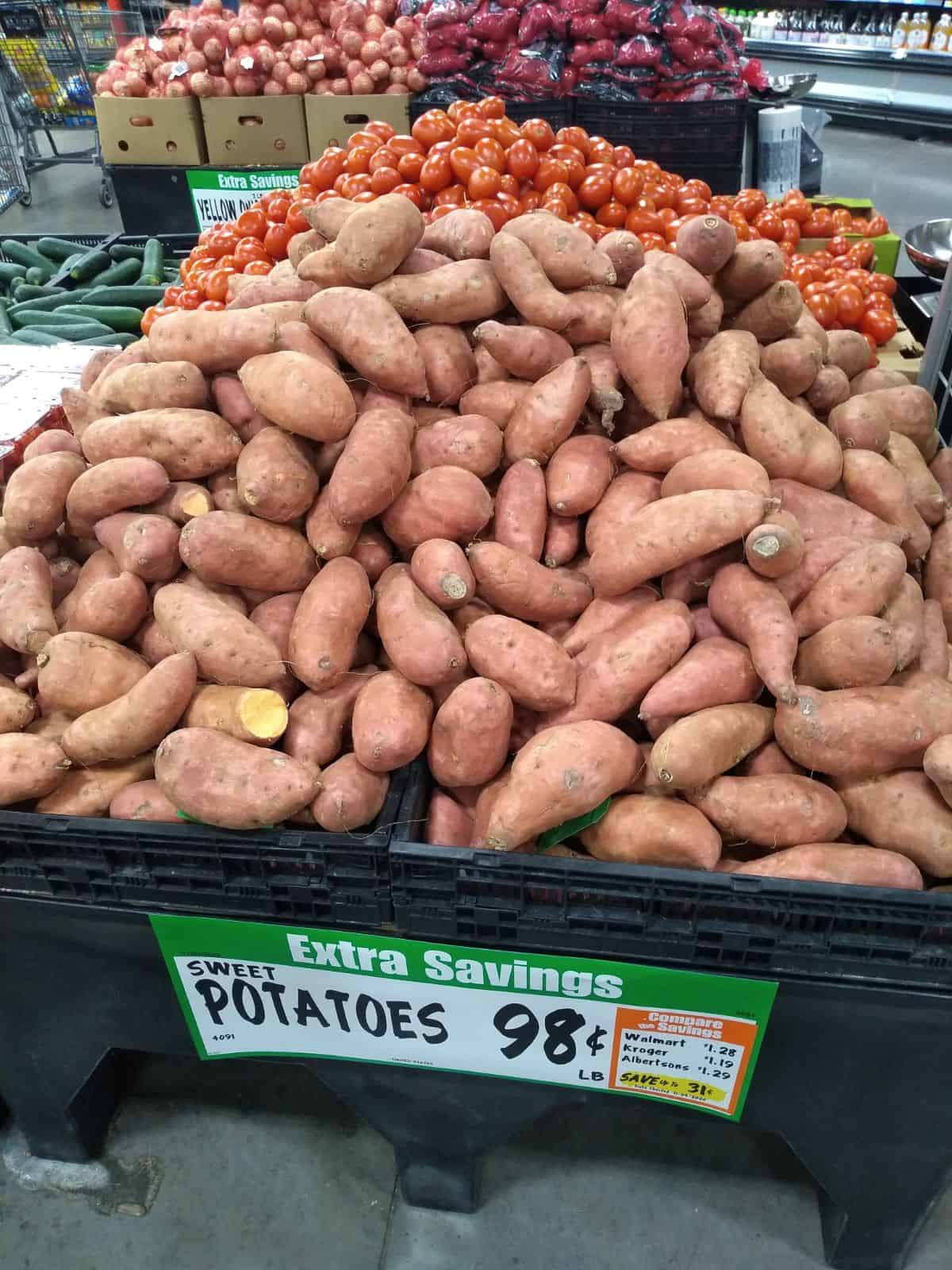 A large black bin of sweet potatoes with a sign saying they are being sold for 98 cents per pound.