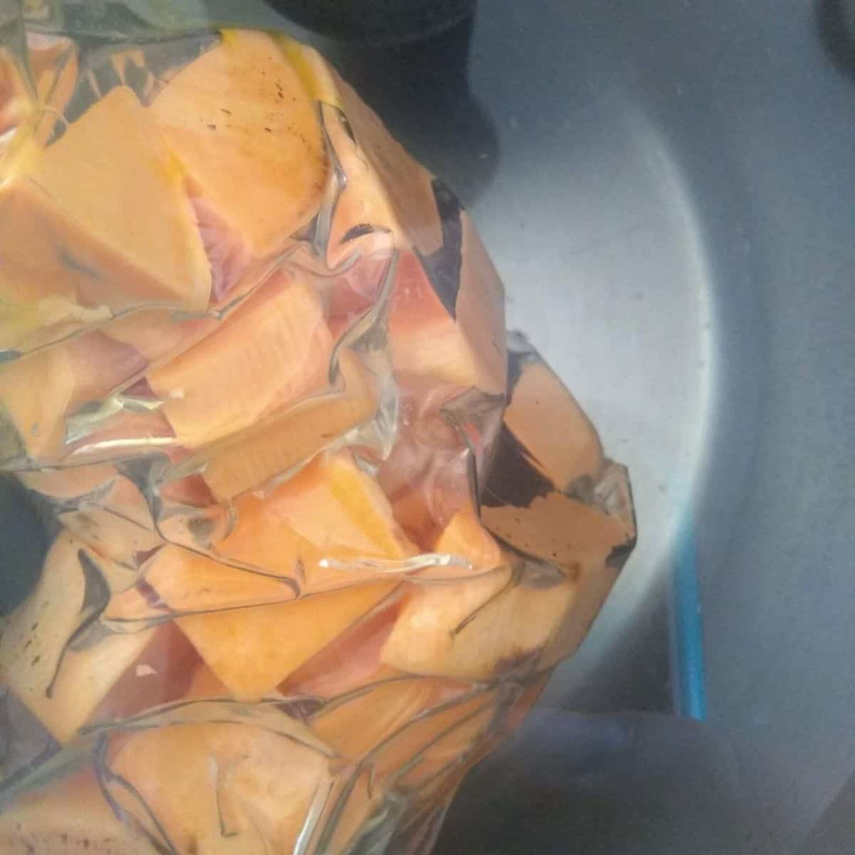 A vacuum sealed bag of orange sweet potatoes in a sous vide watch bath