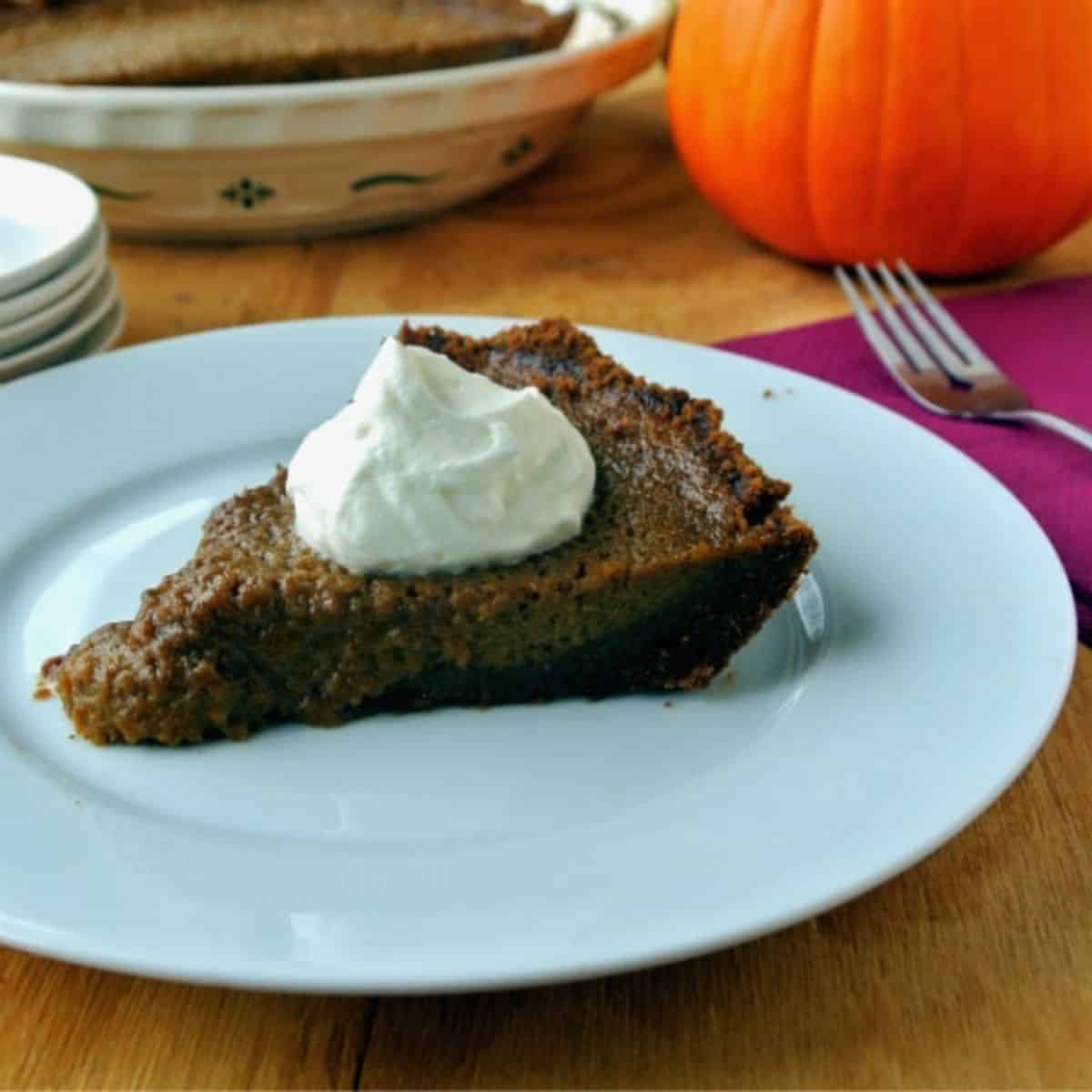 A slice of pumpkin pie sitting on a white plate. A dollop of whipped cream is on top.