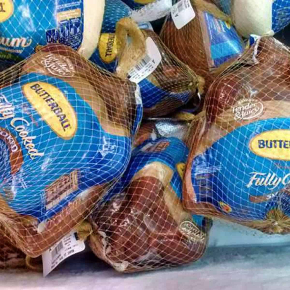 A grocery store display of butterball fully Cooked Smoked Turkeys. the packaging is white, yellow, and shades of brown with a white netting covering all of it. 