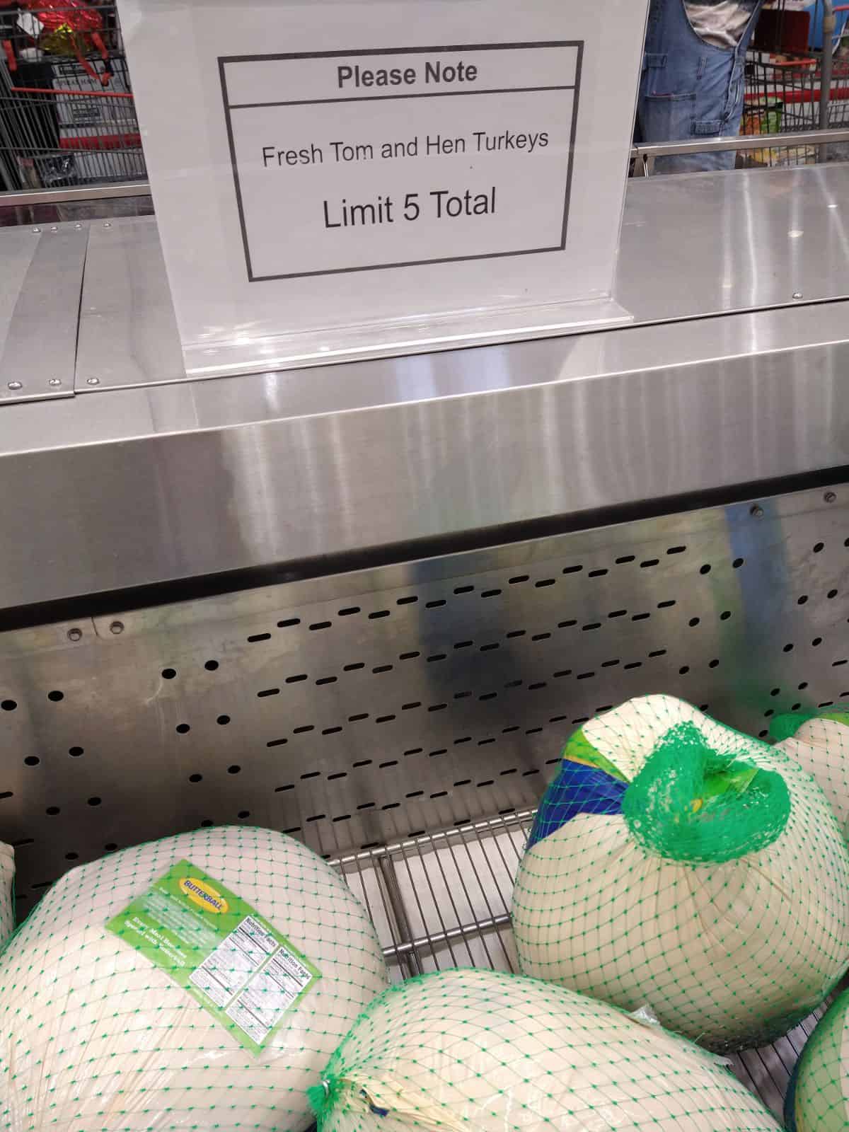 A white sign with black print over top a Costco turkey display says that says Please Note Fresh Tom and Hen Turkeys Limit 5 total. 